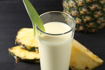 Poster - Tasty pineapple smoothie in glass and fruit on black table, closeup