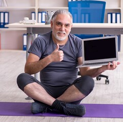 Wall Mural - White bearded old man employee doing exercises in the office