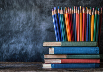 Aufkleber - Stack of colorful books with color pencils standing on a wooden surface on blackboard background