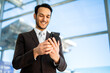 © Minerva Studio - Businessman smiling and using smartphone at airport