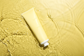 Poster - Tube with cream in water on yellow background, top view. Cosmetic product