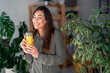 © Dorde - A joyful Caucasian lady sips on fresh orange juice, taking a relaxed pause in her workday, surrounded by contemporary office decor and greenery.