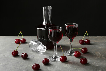 Delicious cherry liqueur in glasses, decanter and fresh berries on grey table