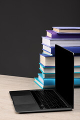 Wall Mural - Stack of colorful books and laptop on white wooden table against black background