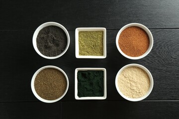 Wall Mural - Different superfood powders in bowls on black wooden table, flat lay