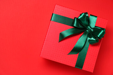 Poster - Gift box with green bow on red background, top view. Space for text