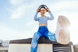 © Iryna - A series of shots of a cheerful sporty woman sitting on a rooftop and enjoying her favorite music halfway through a workout on a sunny rooftop day.