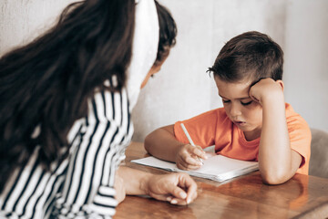 Little school boy doing homework with his mom helping him