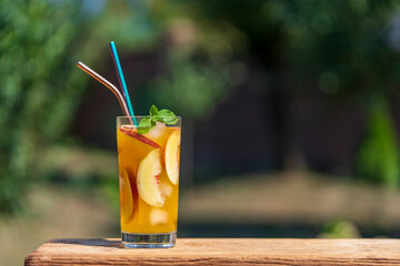 Wall Mural - One glass of a summer cocktail or cold tea with peach slices, ice and mint on the nature background. Closeup, copy space