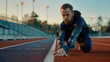 © sommersby - An athlete crouches low on a running track, preparing for a sprint as the sun sets in the background