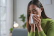 © amnaj - Asian woman having a cold, blowing her nose with a paper tissue, feeling sick and unwell