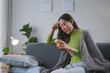 © amnaj - Young asian woman having a headache and taking medicine while sitting on the sofa at home