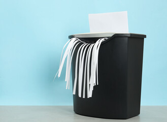 Wall Mural - Destroying sheet of paper with shredder at grey table against light blue background, space for text