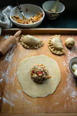 Step by step process of preparing homemade empanadas stuffed with meat, vegetables and quail egg. Rolled dough with filling on wooden board.