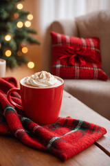 A red cup of cocoa, hot chocolate or coffee with whipped cream on a wooden table with red knitted plaid in front of a Christmas tree. Merry Christmas or New Year concept for banner with copy space.