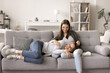 © fizkes - Happy mother rest on comfortable sofa in living room, lying on teenager daughters laps, communicate, smile, enjoy warm relationship, friendship, spend weekend time together. Motherhood, understanding