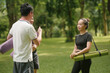 © amnaj - Group of asian people holding yoga mats and talking together in a park before starting their yoga class