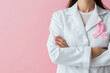 © Alexandra - Doctor with crossed arms wearing pink ribbon on white coat against pink background