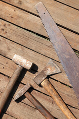 Old tool on a wooden plank surface, top view. Sledgehammer, hammer, ax and hand saw. Old hand tool with rust. Working tool. Master's Day and Father's Day