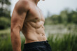 © qunica.com - Close-up of a fit young man with defined abs and muscular build outdoors. Showcasing strength and health in a natural setting.