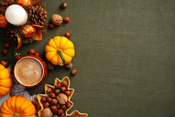 Wall Mural - Autumn flat lay composition with pumpkins, coffee cup, decorative candle with pine cones, leaf-shaped plate with nuts, acorns on green cloth table, top view.