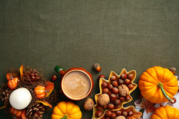 Wall Mural - Still life pumpkins, acorns, candle, coffee cup, decorative leaf-shaped plate with nuts on green cloth table. Autumn, fall, Thanksgiving concept. Flat lay, top view.
