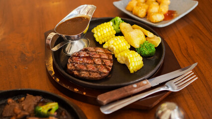 close up of beef steak and blackpaper sauce with corn, broccoli and boiled potatoes on a wooden table