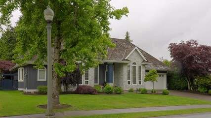 Wall Mural - Establishing shot of two story stucco luxury house with big tree and nice landscape at spring rainfall in Vancouver, Canada, North America. Day time on June 2024. ProRes 422 HQ.