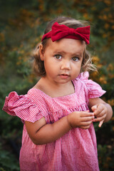 Close up. Portrait of cute baby girl in a red checkered dress with a red bow on her head outdoor.