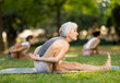 © JackF - Aged lady in sportwear with group of sporty adult people training stretching workout legs at light city park together