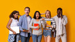 © Prostock-studio - Exams time. Stressed group of multiethnic students with books holding alarm, yellow background, panorama