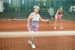 © JackF - Focused elderly woman in action during tennis game on clay court, playing doubles with young female partner captured in background, showcasing fitness and teamwork