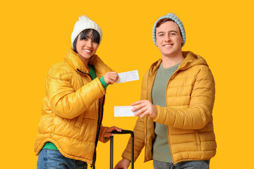 Poster - Beautiful young happy couple with suitcase and tickets on yellow background. Winter vacation concept