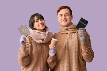 Poster - Beautiful young happy couple with passports and cup of coffee on purple background. Winter vacation concept