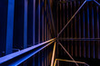 © Emvats - A close-up, abstract view of metal beams and structures illuminated with blue and yellow lights. The geometric lines and contrasting colors create a modern, industrial aesthetic.