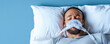 © Rutchaneewan - Man in bed wearing a CPAP mask, eyes closed, resting on white pillows, serene expression against a calming blue background, emphasizing sleep health and comfort.