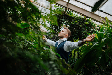 Wall Mural - Handsome businessman standing in botanical garden, in the middle of lush green foliage, arms open. Concept of corporate social responsibility and ESG.