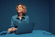© Jacob Lund - Mature businesswoman smiling and looking away while working on laptop and smartphone in monochromatic studio shot