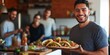 © Iryna - A man is holding a plate of food in front of a group of people. The man is smiling and he is happy. The food on the plate is a variety of tacos