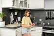 © Westend61 - Smiling girl using smart phone in kitchen at home