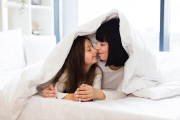 Wall Mural - Warmth, love, family connection. Mother and daughter lying in bed and playing, covered with blanket as in house.