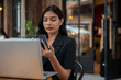 © bongkarn - An attractive Asian businesswoman is using her smartphone while working remotely from a cafe.