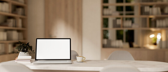 Wall Mural - A laptop computer with a white-screen mockup on a white marble table in a contemporary cozy room.