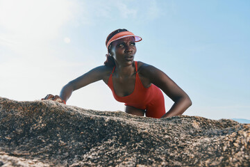 Active woman climbing a rocky surface against a clear blue sky in a bright red athletic outfit