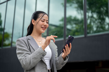 Wall Mural - A smiling businesswoman is reading messages or chatting on her smartphone while walking in the city.