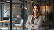 © JINGWEN - Confident businesswoman with crossed arms smiling in modern office, facing camera, embodying success in professional attire with sleek hairstyle.