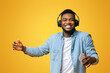 © Prostock-studio - Happy black guy in wireless headphones listening music on smartphone and dancing, yellow studio background with free space