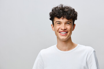 Young man with curly hair smiling brightly in a minimalistic setting, wearing a plain white t shirt, ideal for various lifestyle and portrait themes