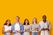 © Prostock-studio - Group of surprised multinational students with smartphones looking at empty space over yellow background, new mobile app for studying