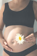 © puhimec - Close-up of pregnant woman holding white daisy flower near her big belly.